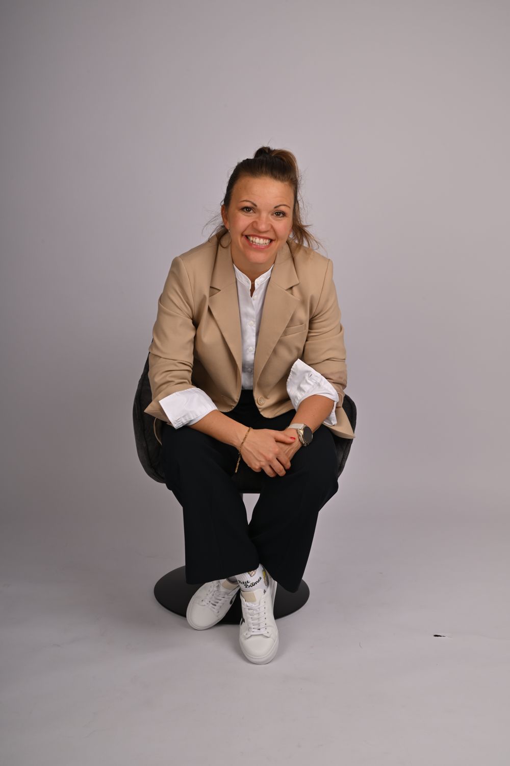 Steffi Reith im beigen Blazer, lachend nach vorne gebeugt auf einem Stuhl sitzend